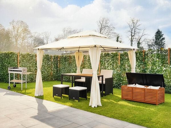 Outdoor garden setup featuring a cream gazebo with curtains, a dining table and chairs, stools, a barbecue trolley, and a wooden storage box on a green lawn. Click to see the products in the collection.